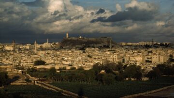 A modern city surrounds a height overlaid by ruins